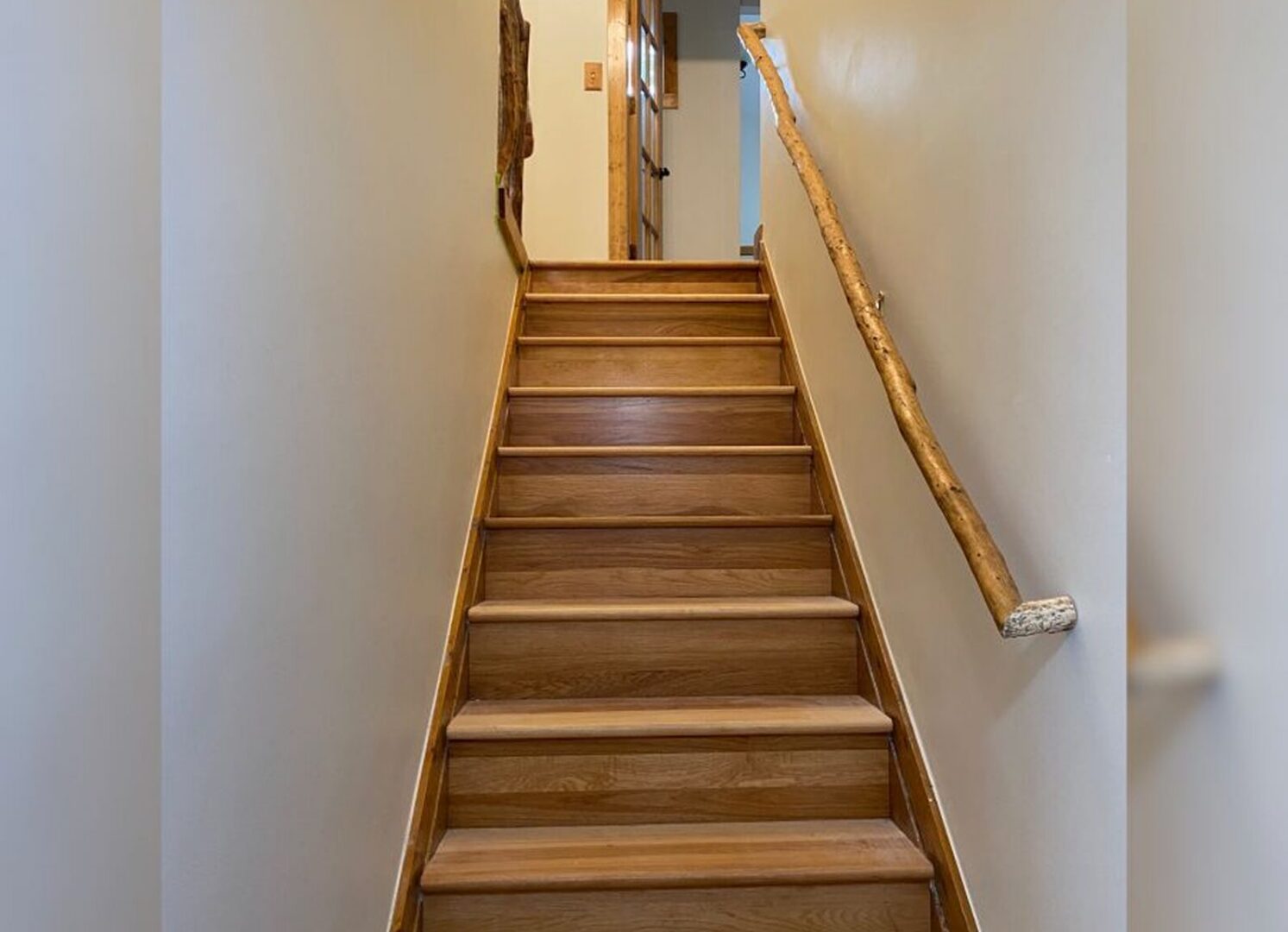 Wooden staircase with a wooden handrail in a home, with a wall on the left side