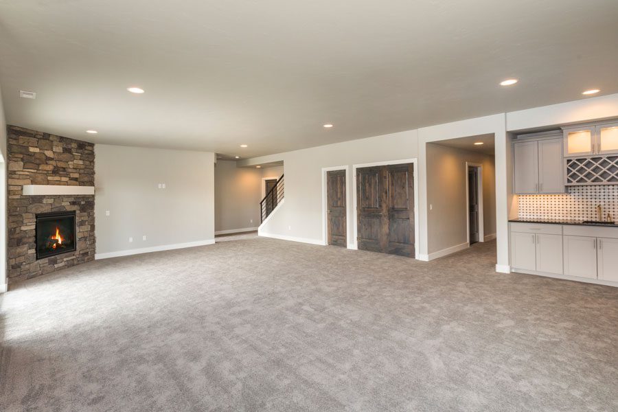 Living room with a carpeted floor, a fireplace on the left side, doors, a staircase, a railing, cupboards, a countertop