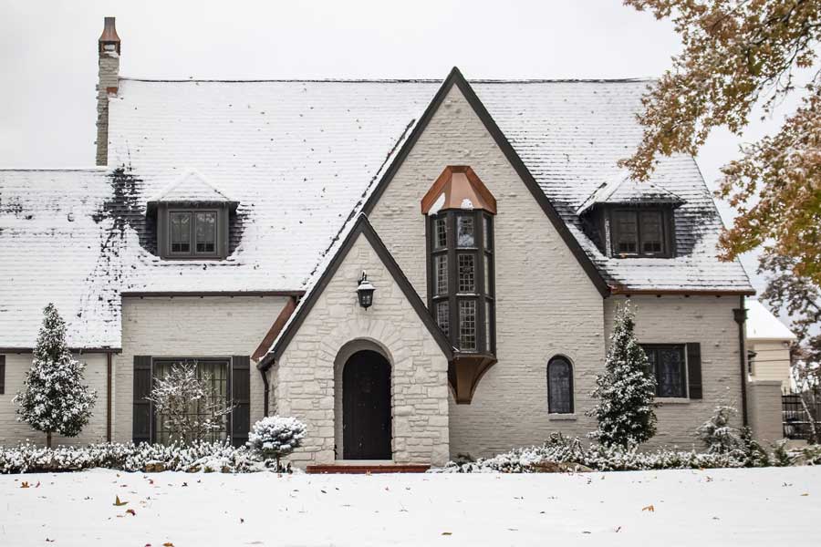 White house with a black door and windows, surrounded by plants and trees