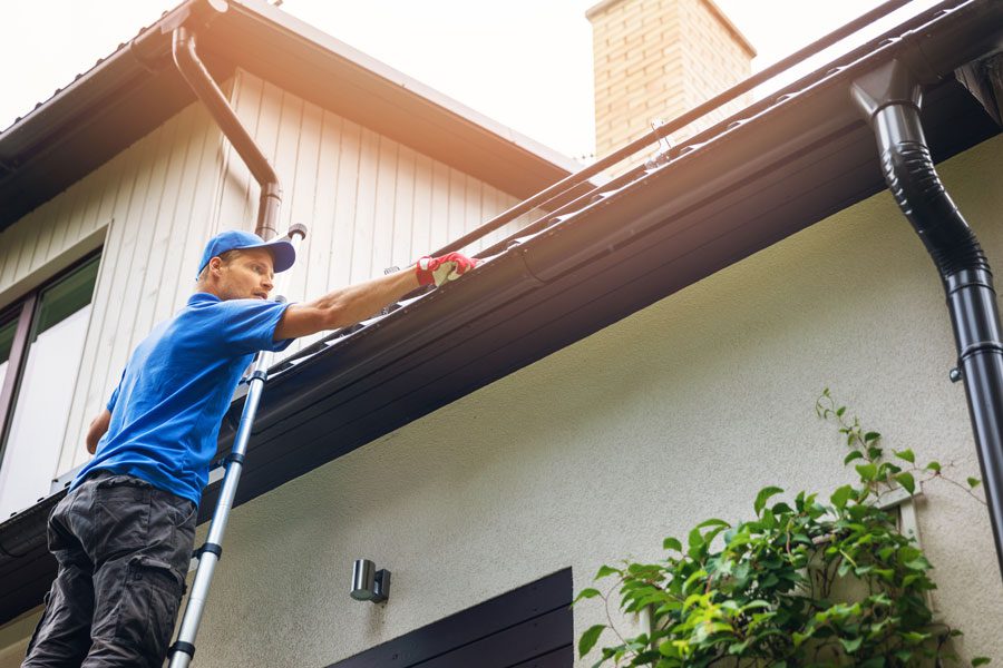 Man on a ladder cleaning the gutters of a house in, CA