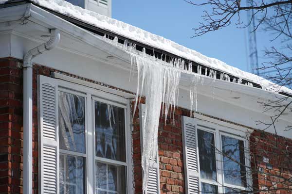 House with windows covered in snow and icicles hanging from the roof