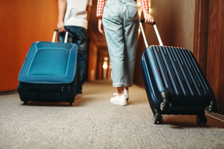 Two people walking down a hallway with their luggage, illuminated by lights in the background
