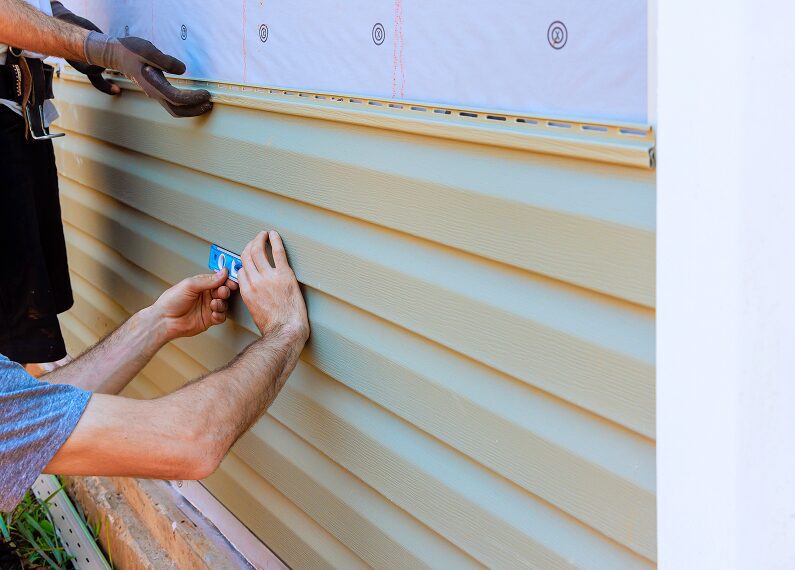 Man wearing gloves and holding a tool while installing siding on the side of a house