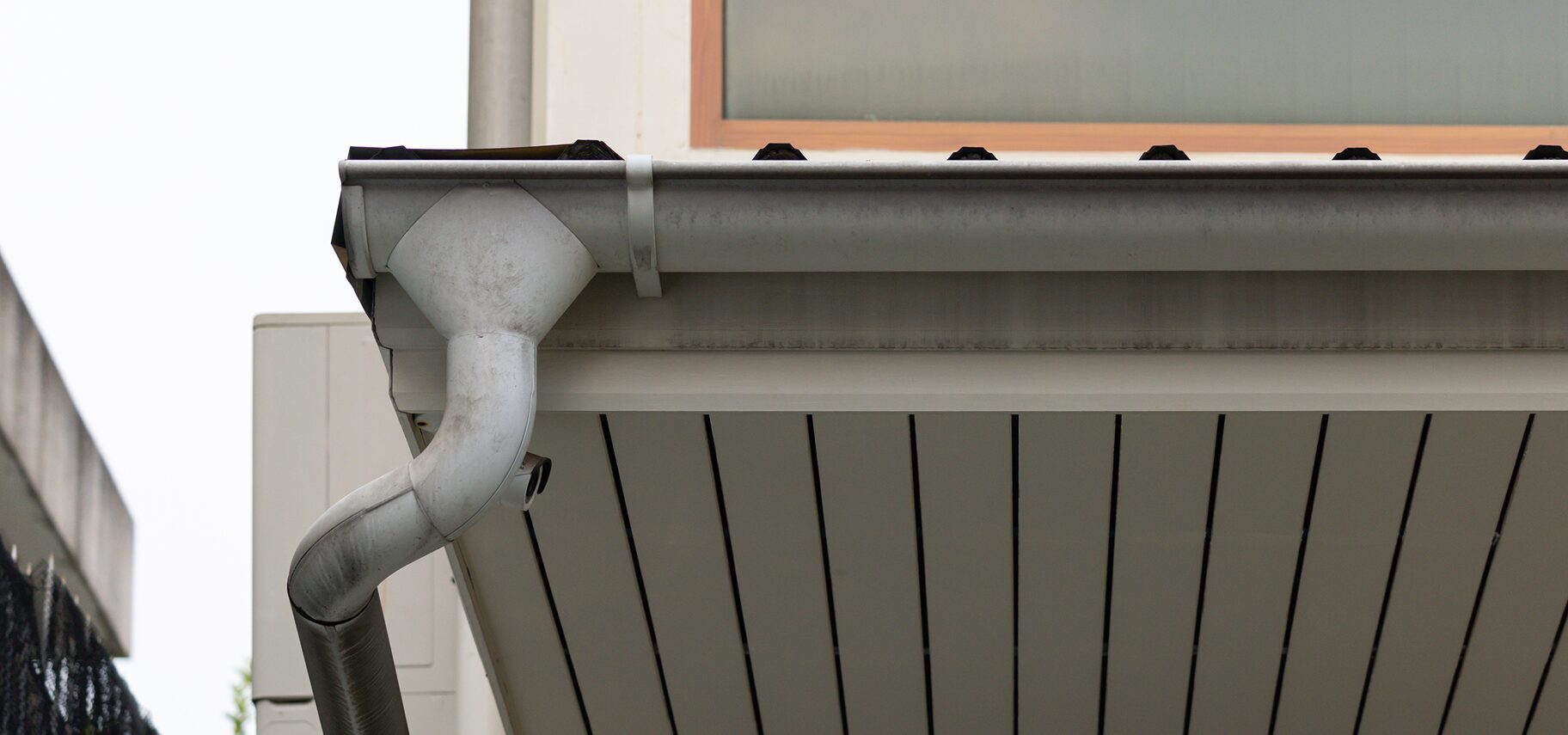 Building with a window and a metal gutter on the side of it, with a wall on the left side