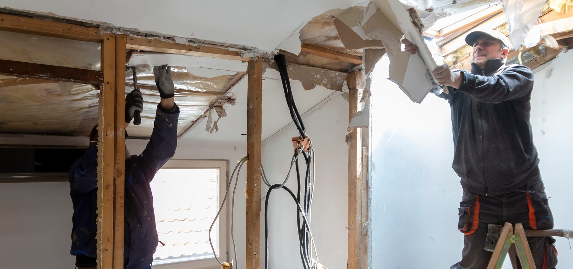 Two men working on a wall in a room