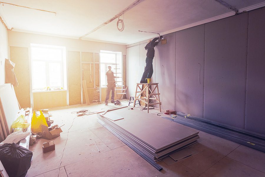 Two men working on a wall in a room that is being remodeled