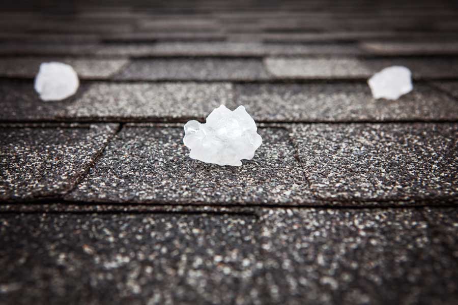 Roof of a house in with hail scattered across it, indicating that the roof is in need of repair