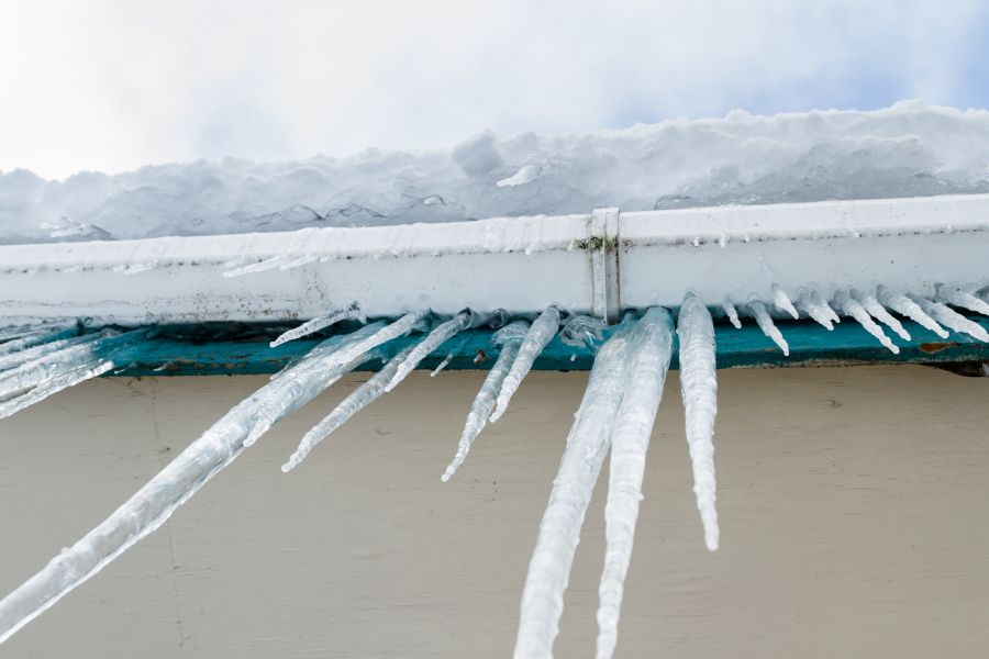 Icicles hanging from the roof of a house, with snow in the background and a clear sky above