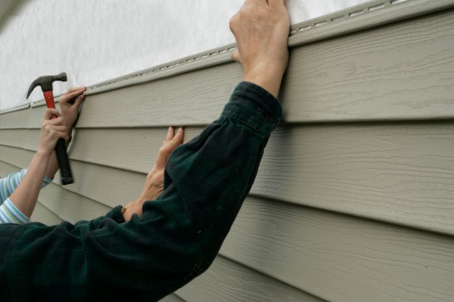Man using a hammer to remove siding from a house