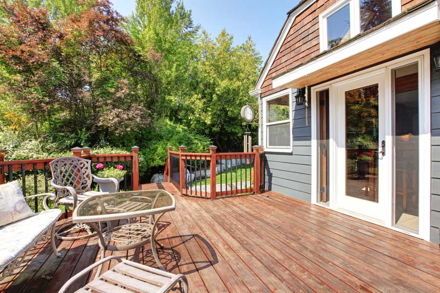 House with glass doors and windows, a wooden deck with a table and chairs on it, a sofa with pillows