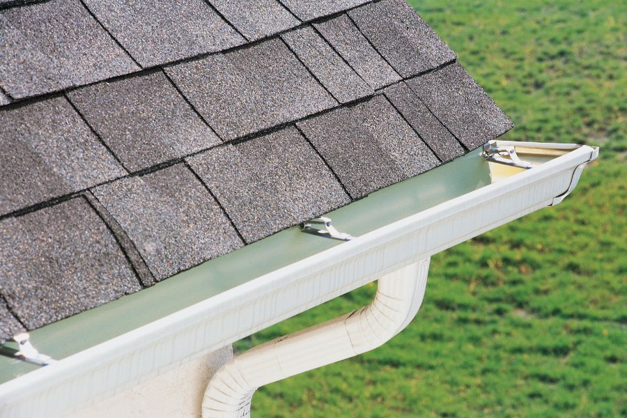 Roof of a house with a gutter running along the side of it, and a pipe running along it
