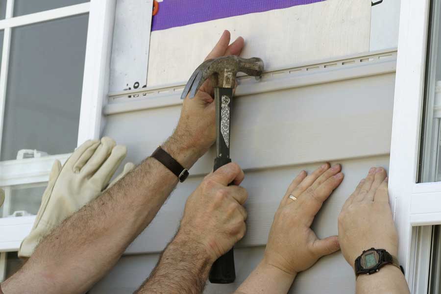 Two men working on a window with a hammer, installing siding