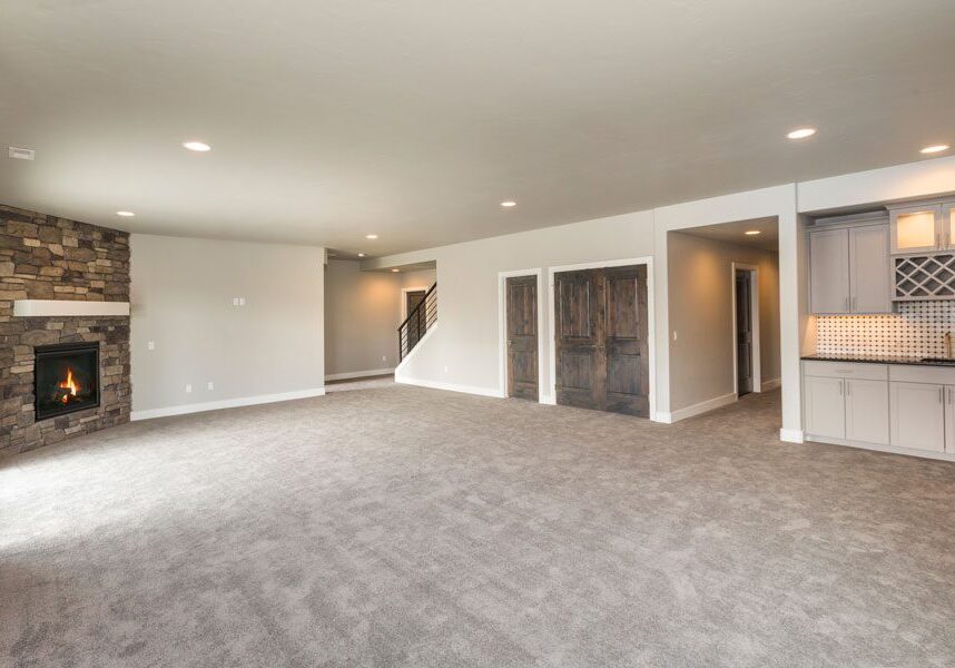 Living room with a carpeted floor, a fireplace on the left side, doors, a staircase, a railing, cupboards, a countertop