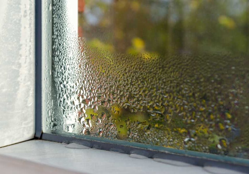 Close up of a window with water droplets on it, set against a blurred background