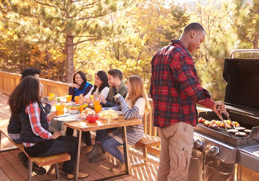 Group of people gathered around a table on a deck, enjoying a meal together