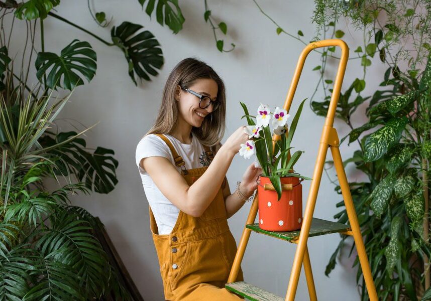 Woman sitting on a ladder, holding a potted plant in her hands and She is surrounded by lush green plants