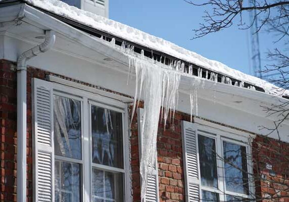 House with windows covered in snow and icicles hanging from the roof