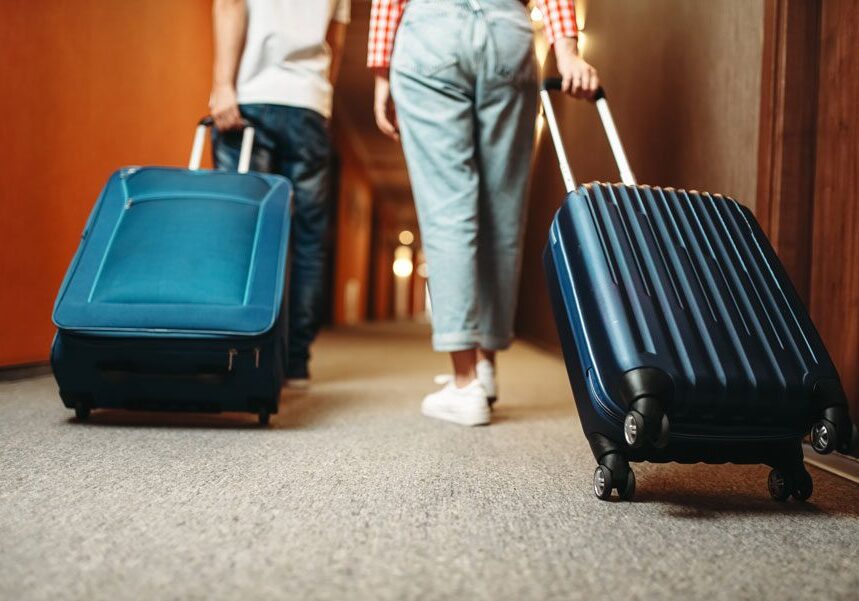 Two people walking down a hallway with their luggage, illuminated by lights in the background