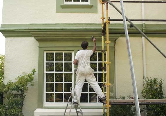 Man on a ladder painting the side of a house