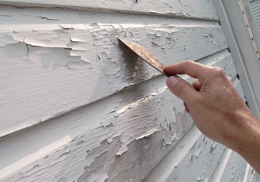 Person using a knife to remove paint from a house siding, likely to repair the siding
