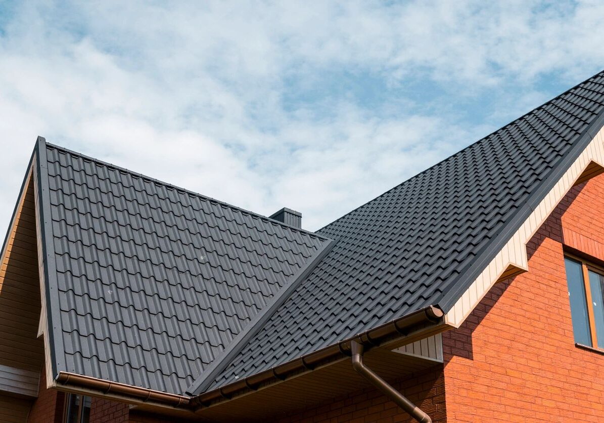 Brick house with a metal roof and windows, and in the background there is a sky with clouds