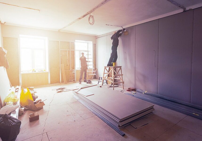 Two men working on a wall in a room that is being remodeled