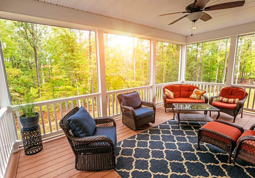 Screened porch with wicker furniture, including sofas with pillows, chairs, a table, and a carpet on the floor
