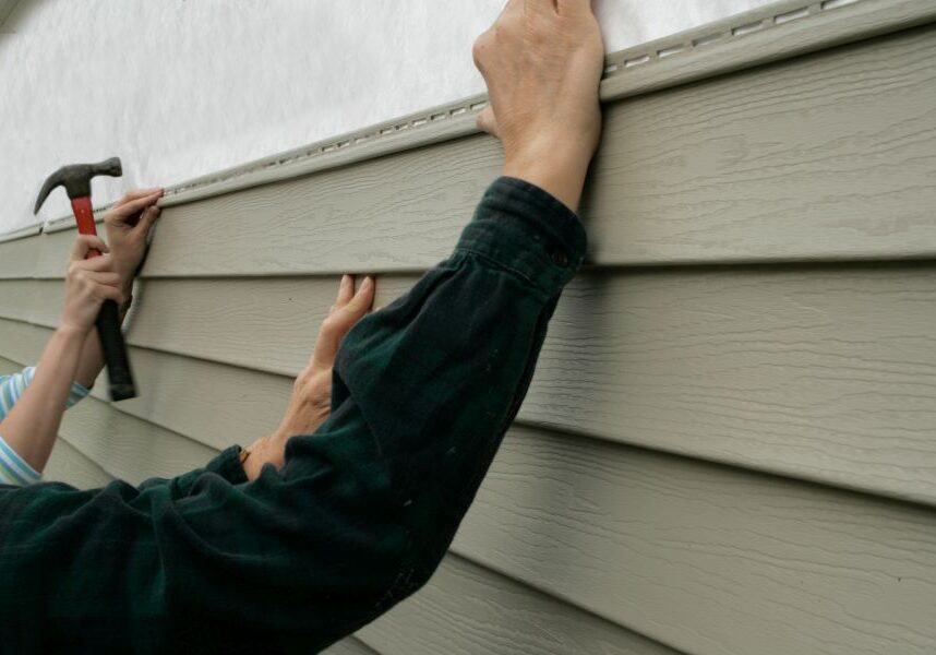 Man using a hammer to remove siding from a house