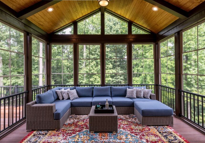 Screened porch with a couch and pillows, a table with bottles and other objects, a carpet on the floor, railings